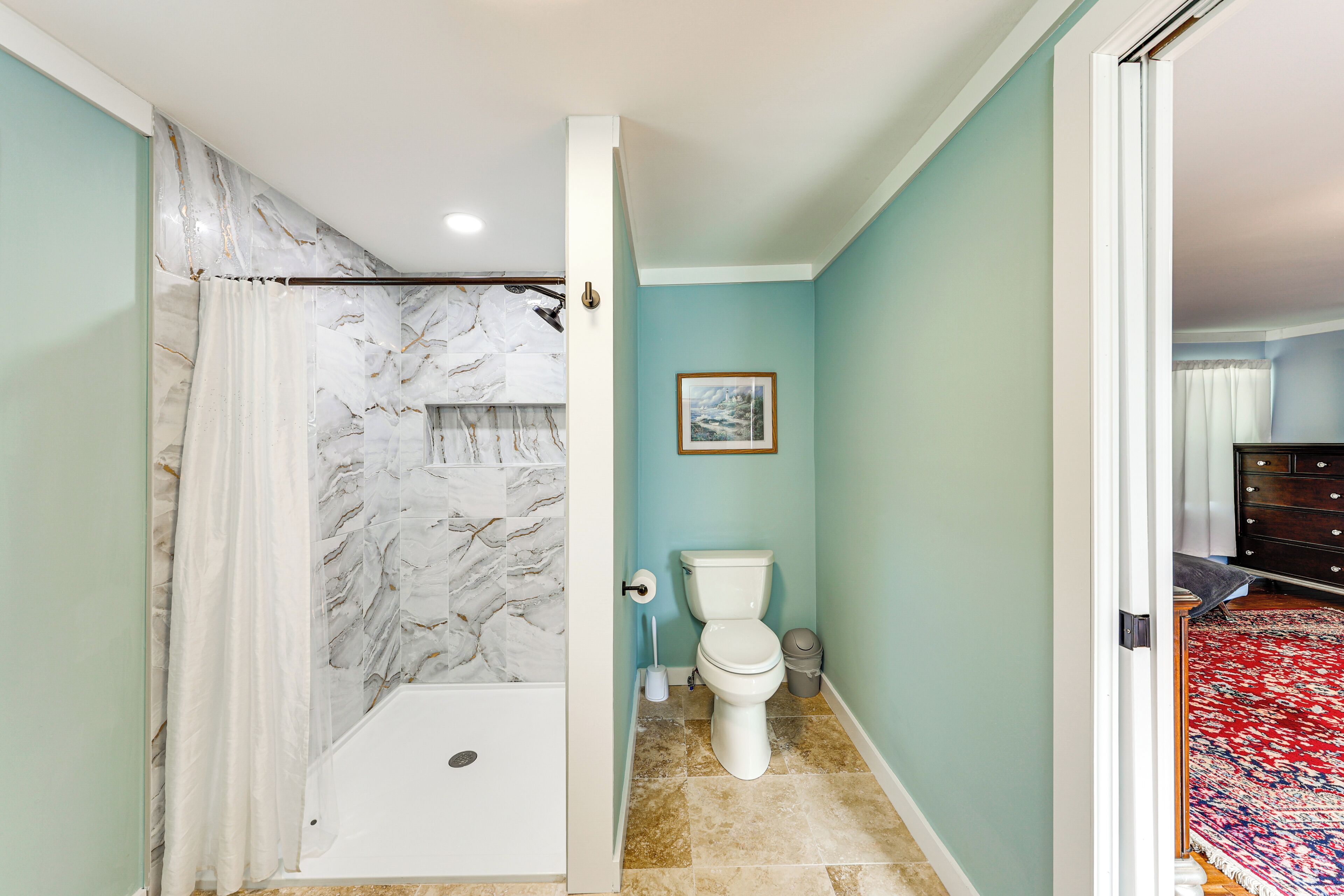 A bathroom with a shower, toilet, and a marble wall.