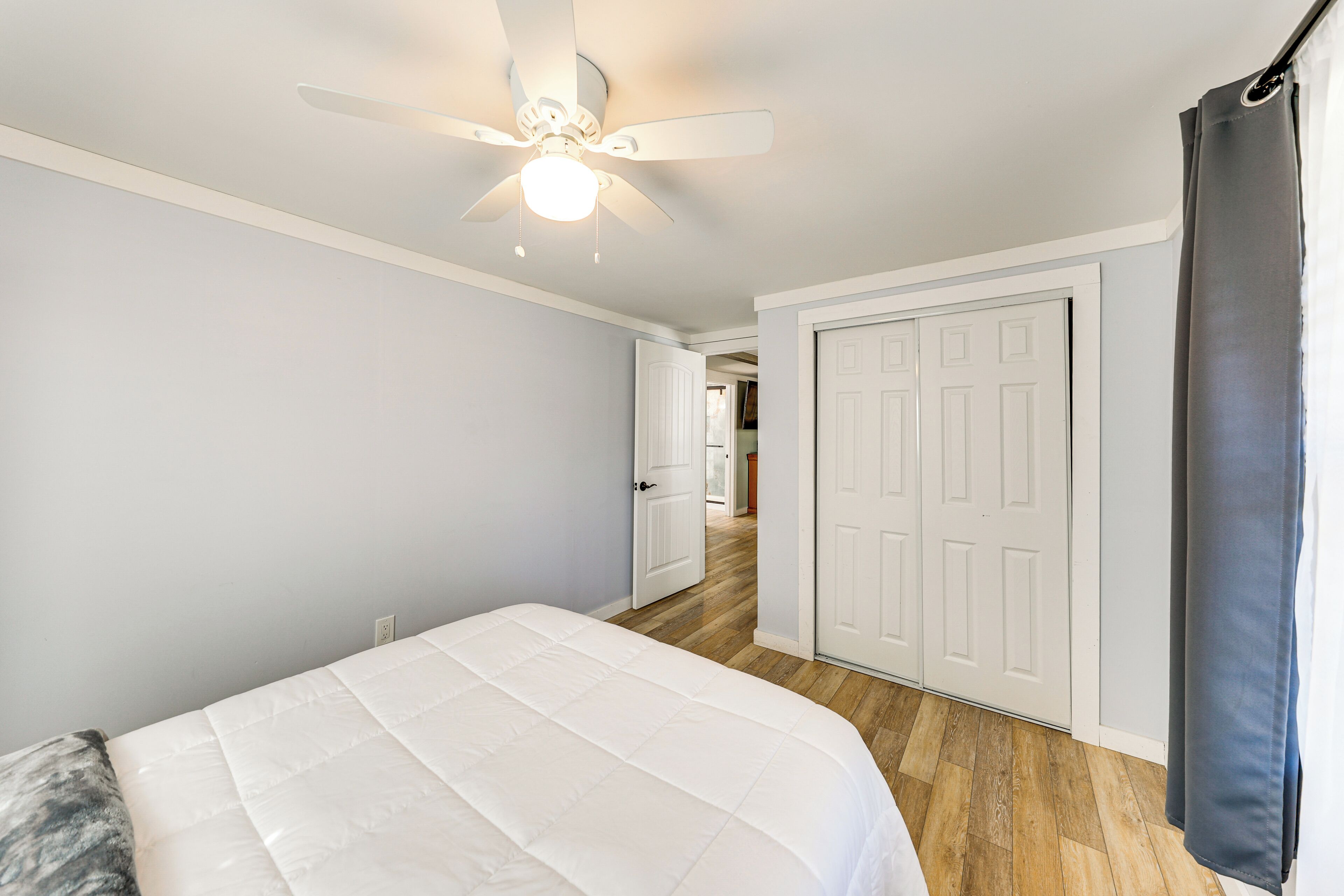 A bedroom with a bed, a ceiling fan, and a door leading to another room.