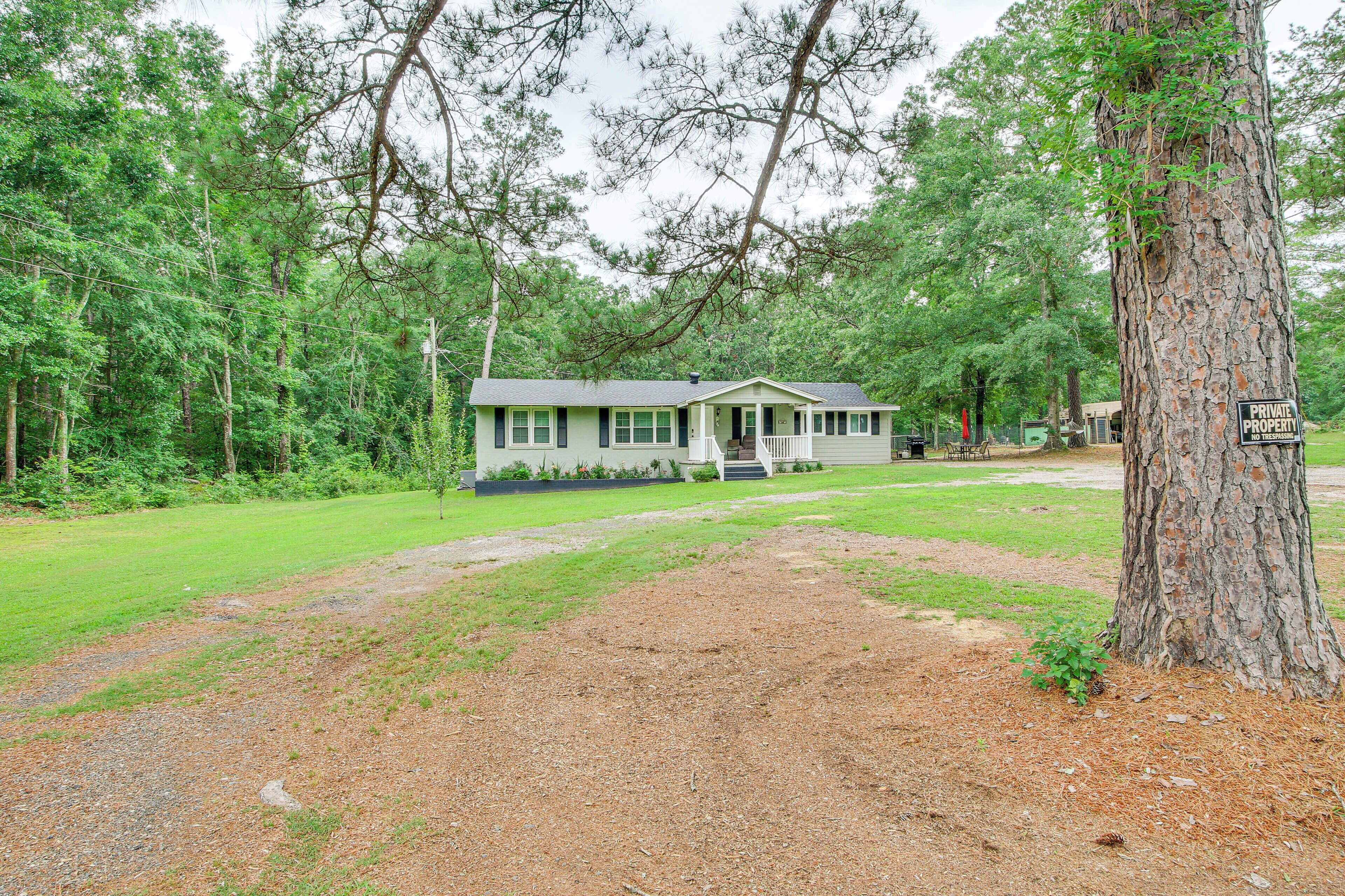 Eenlaags huis met veranda, omringd door bomen en een gazon.