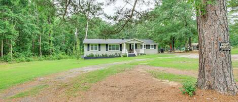 A single-story house with a porch, surrounded by trees and a grassy yard.