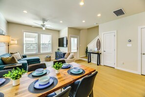 A modern living room with a wooden dining table set for four, a blue sofa, a ceiling fan, and a staircase leading to another level. - 1 Mi to Beach: Home w/ Pool Access in Port Aransas (Port Aransas)