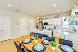 A modern kitchen with white cabinets, a central island, and a dining area with a wooden table and black chairs. - 1 Mi to Beach: Home w/ Pool Access in Port Aransas (Port Aransas)