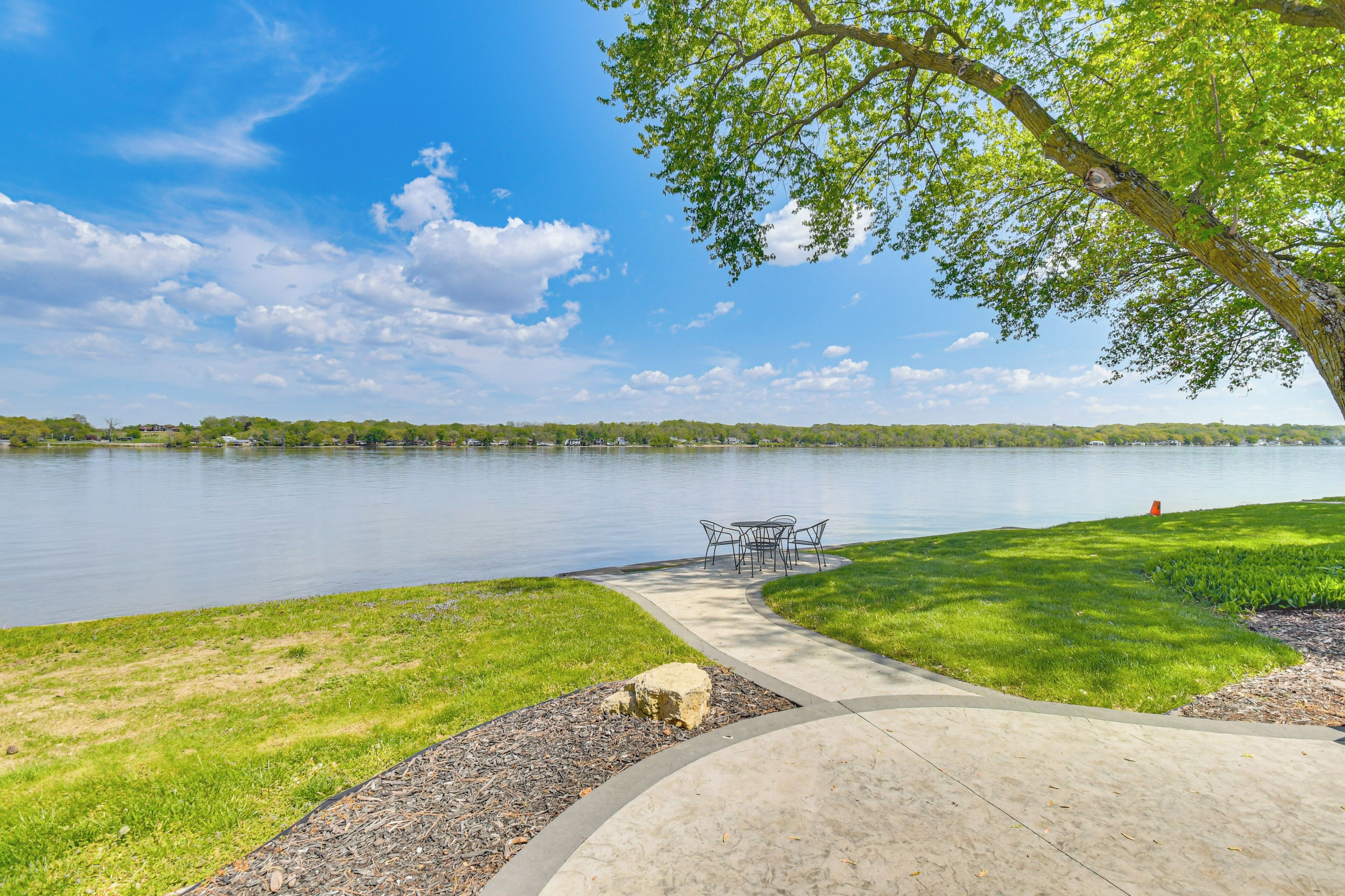 A lakeside park with a concrete pathway, a picnic table, and a grassy area.