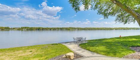 A lakeside park with a concrete pathway, a picnic table, and a grassy area.