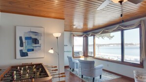 Een kamer met een tafelvoetbaltafel, een tafel met stoelen, een groot raam met uitzicht op de zee en een emmer met de tekst 'VOOR HOT TUB'.