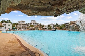 Una piscina con un saliente rocoso, varios edificios y una cascada.