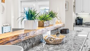 Ett kök med en bänkskiva i granit, tre krukväxter, en korg av rotting och vita skåp.