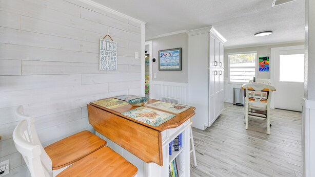 A kitchen with a wooden table, white cabinets, and a white chair. - Fish, Swim & Unwind: Anna Maria Apt Steps to Beach (Anna Maria)