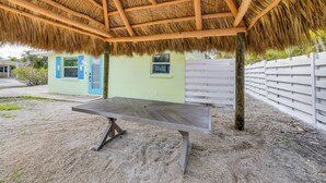 A covered outdoor area with a wooden table and a thatched roof. - Fish, Swim & Unwind: Anna Maria Apt Steps to Beach (Anna Maria)