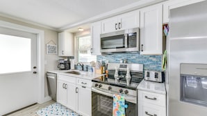 A modern kitchen with white cabinets, stainless steel appliances, a tiled backsplash, and a wooden floor. - Fish, Swim & Unwind: Anna Maria Apt Steps to Beach (Anna Maria)