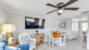 A living room with a sofa, chairs, a coffee table, a TV, and a ceiling fan. - Fish, Swim & Unwind: Anna Maria Apt Steps to Beach (Anna Maria)