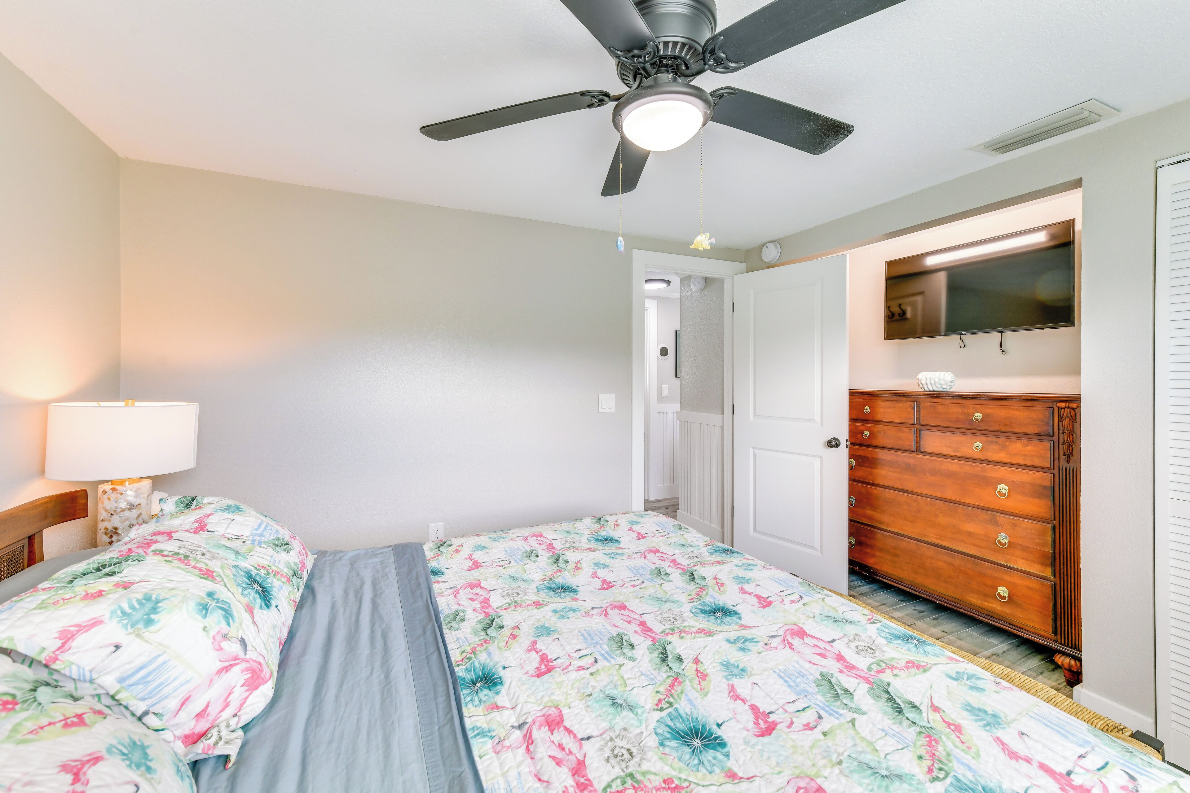 A bedroom with a bed, a ceiling fan, a dresser, and a television mounted on the wall.