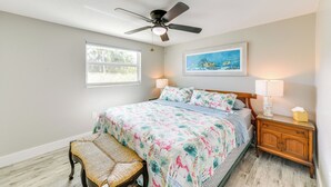 A bedroom with a bed, bedside table, nightstand, ceiling fan, and a window. - Fish, Swim & Unwind: Anna Maria Apt Steps to Beach (Anna Maria)