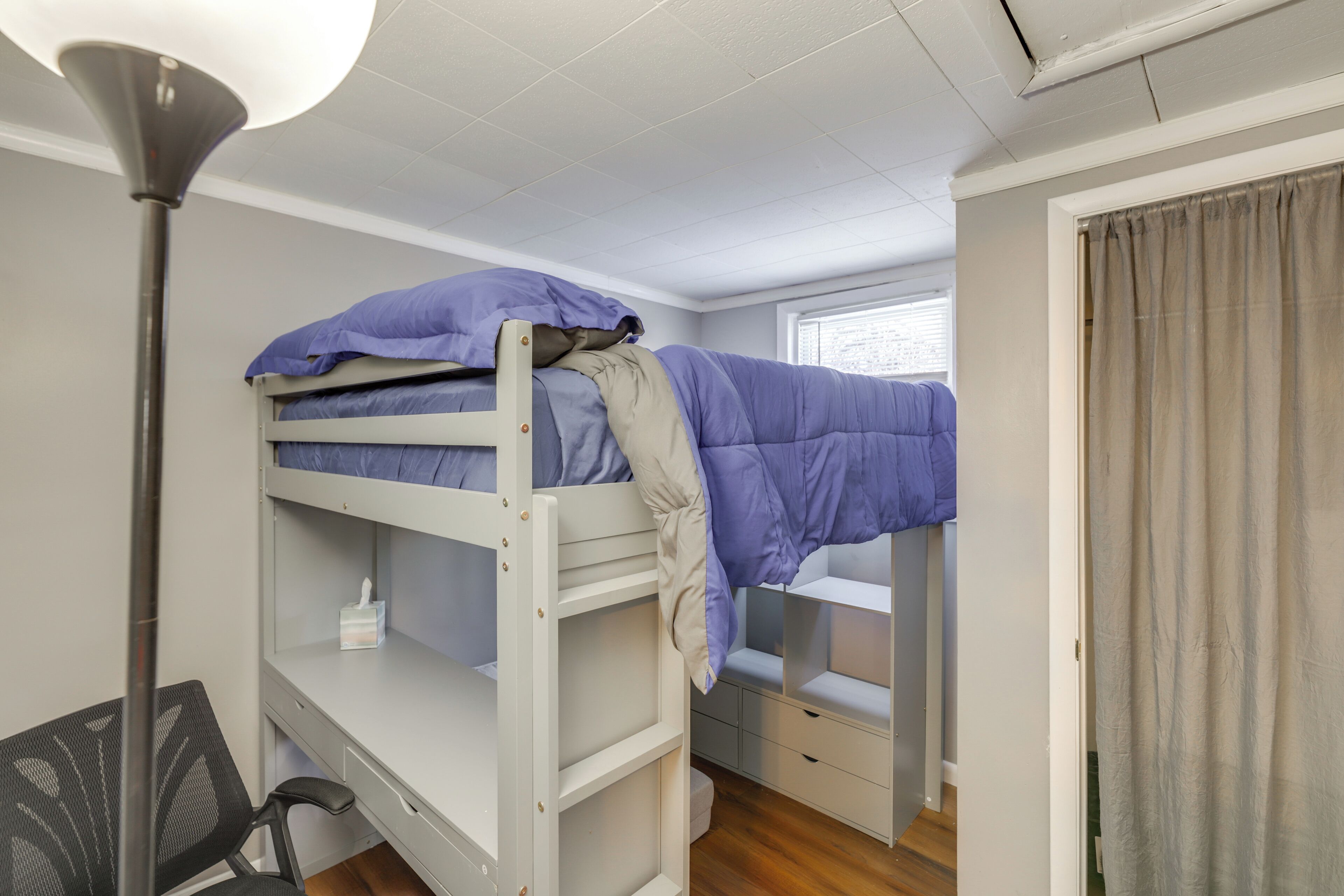A bunk bed with a desk and chair, a lamp, and a window with curtains.
