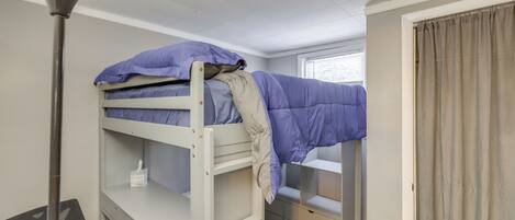 A bunk bed with a desk and chair, a lamp, and a window with curtains.