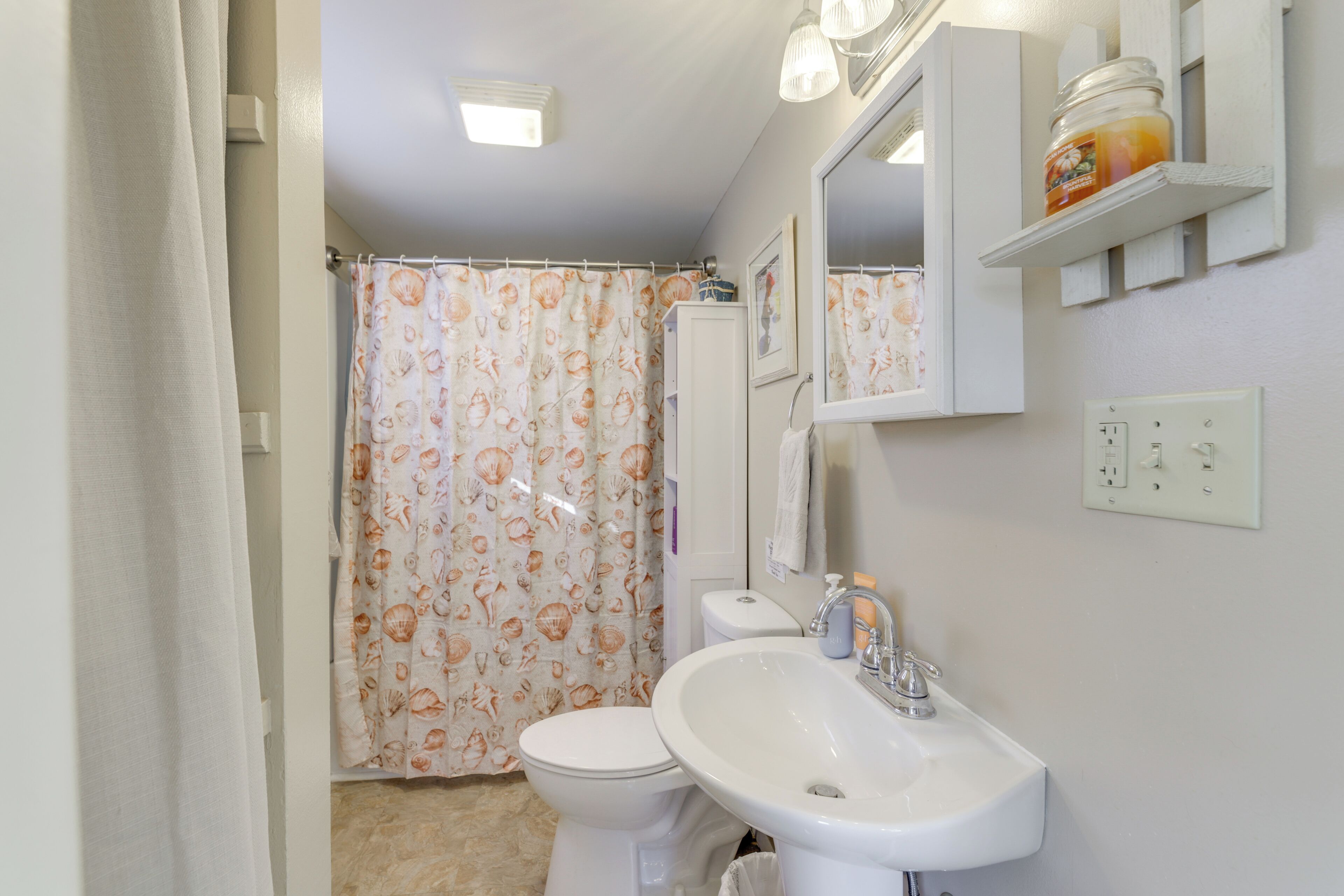 Een badkamer met toilet, wastafel en douchegordijn met schelpenprint.