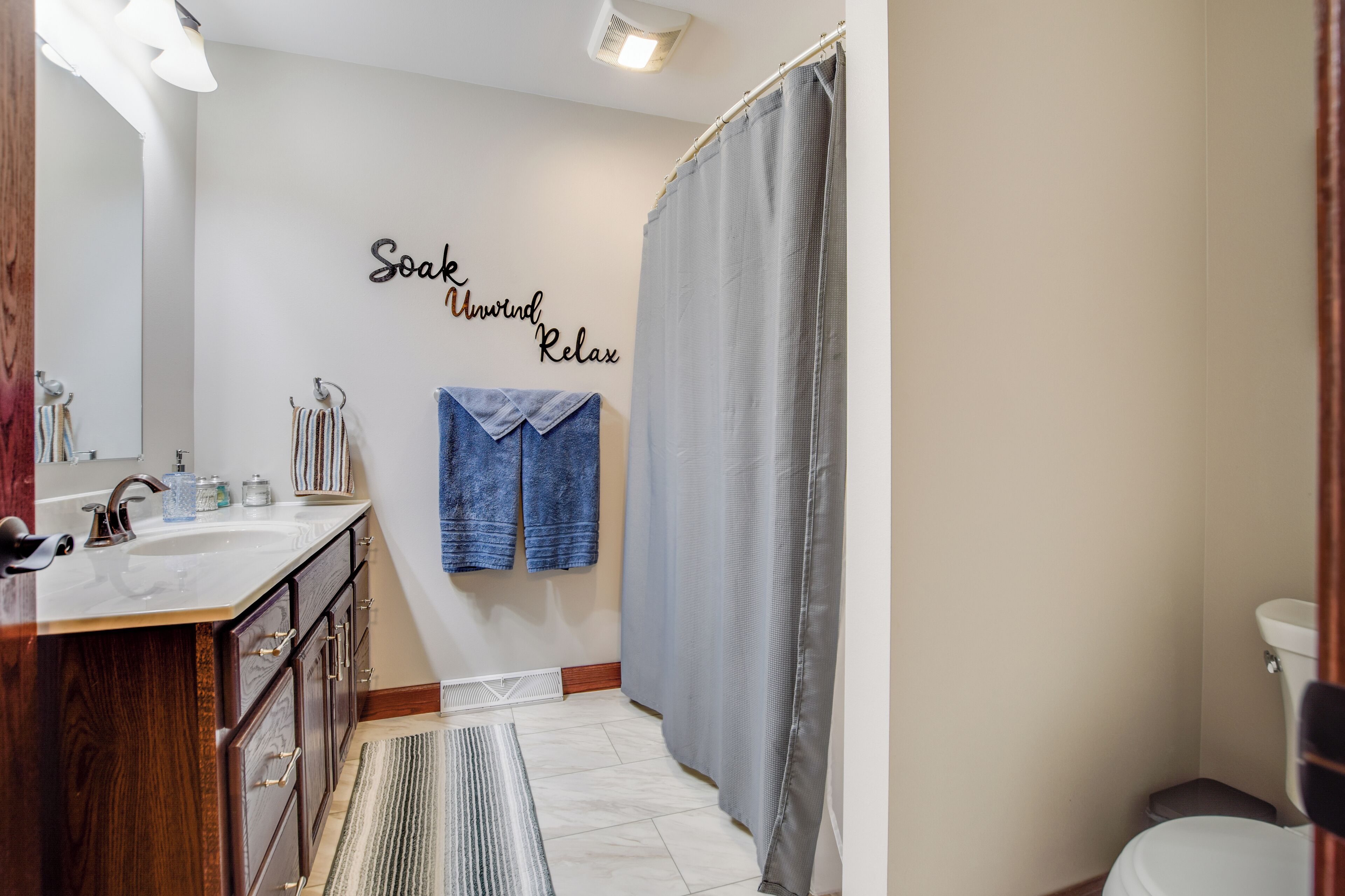 A bathroom with a wooden vanity, a white sink, a towel rack with a blue towel, and a shower curtain.