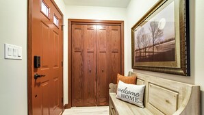 A hallway with a wooden door, a bench with a 'welcome home' pillow, and a framed landscape picture on the wall. - 2026-NEW BOOKING SPECIAL at The Belvedere just Steps to downtown. (New Glarus)