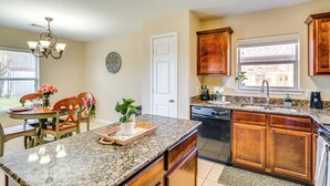 A kitchen with granite countertops, wooden cabinets, a dishwasher, and a dining area with a table and chairs. - Suburban Home in Magnolia w/ Fenced Yard (Magnolia)