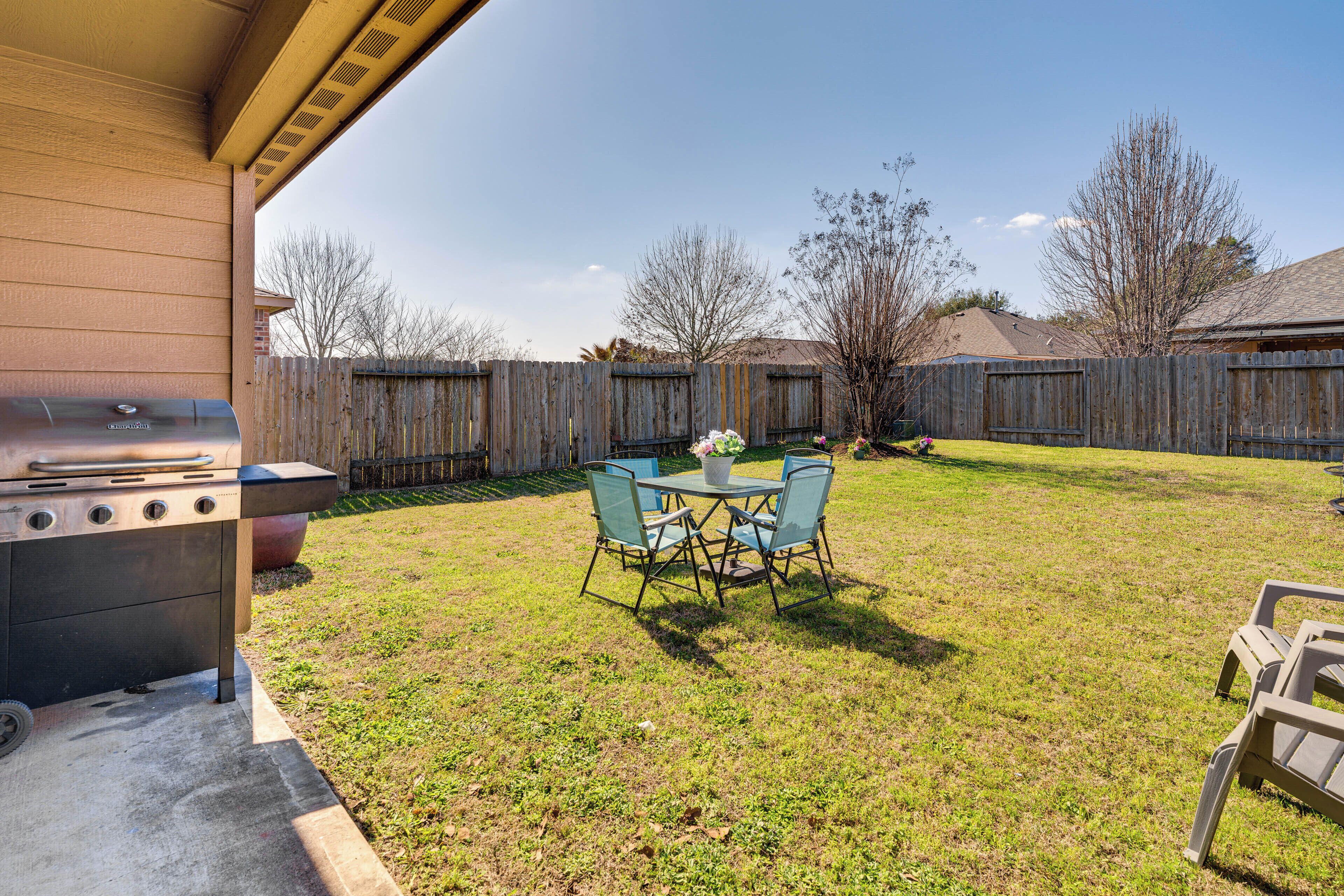 Un jardin avec un barbecue, une table et des chaises, et une clôture en bois.