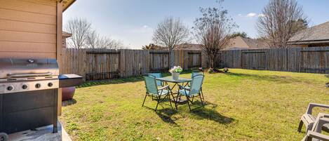 Un jardin avec un barbecue, une table et des chaises, et une clôture en bois.