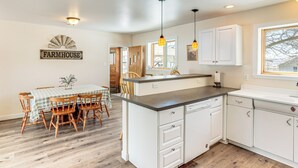 Una cocina con armarios blancos, un letrero de estilo campestre y un comedor con sillas y mesa de madera.