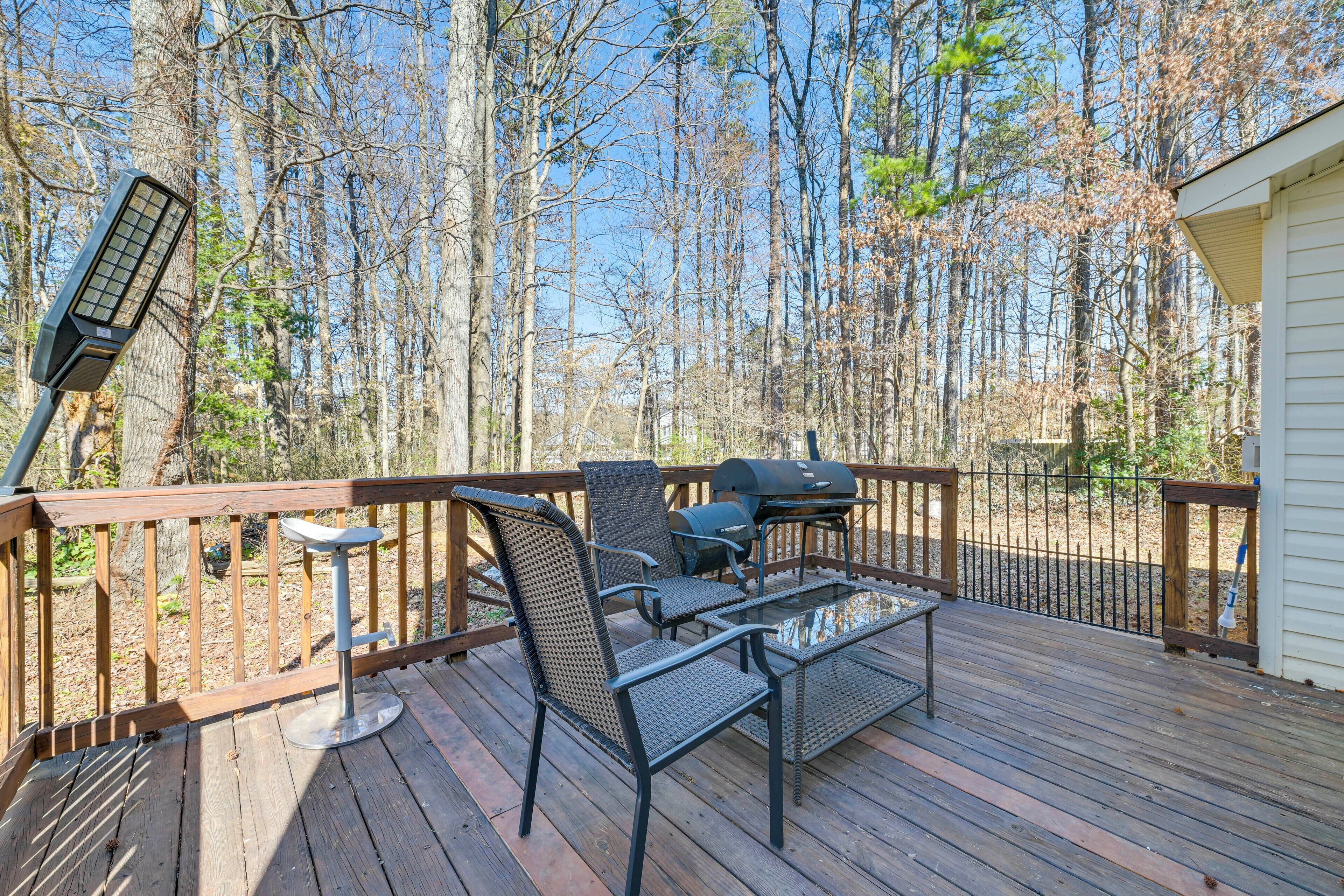 A wooden deck with outdoor furniture, including chairs and a table, overlooking a forested area.