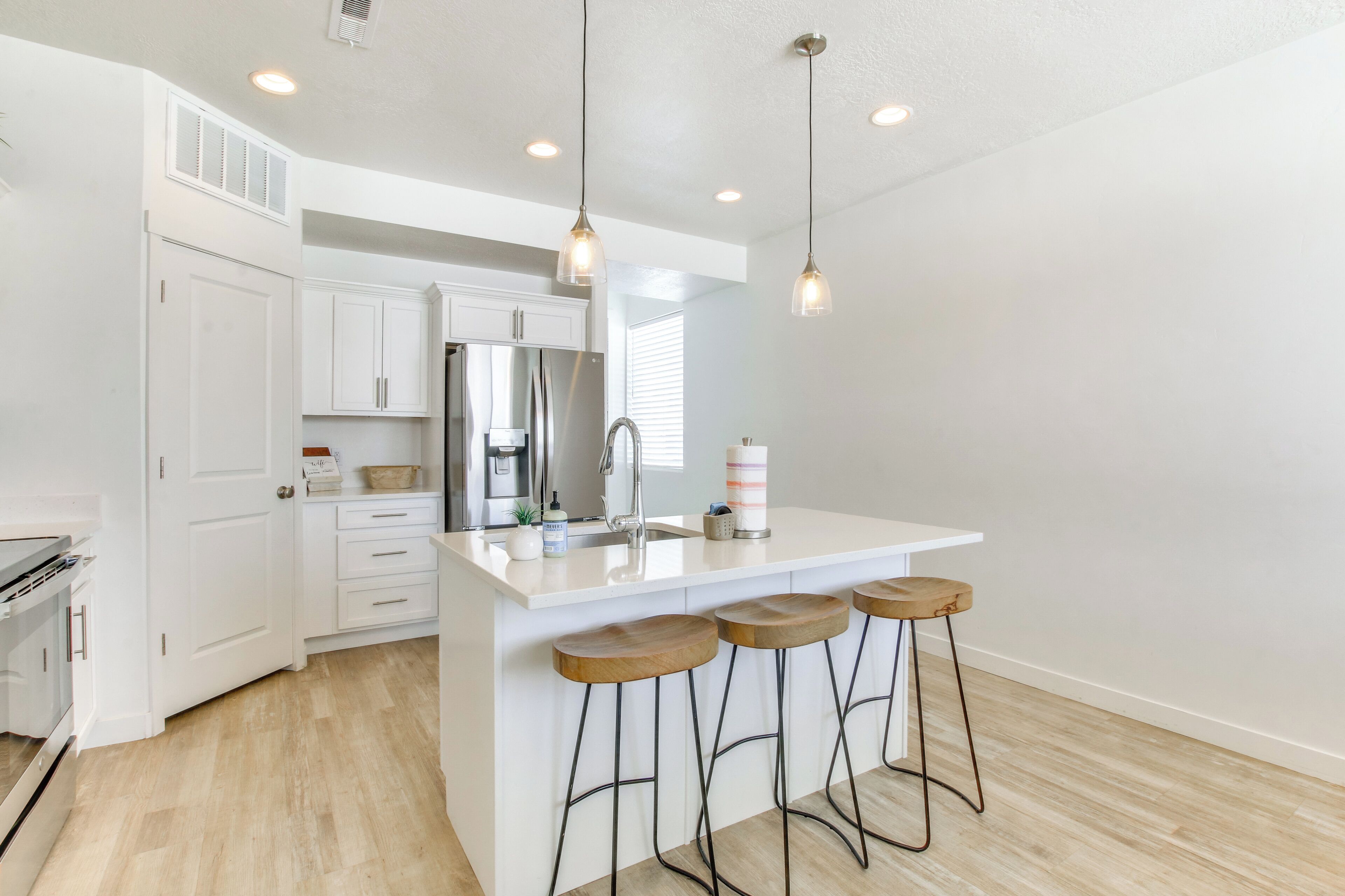 A modern kitchen with white cabinets, a stainless steel refrigerator, a sink, and wooden bar stools.