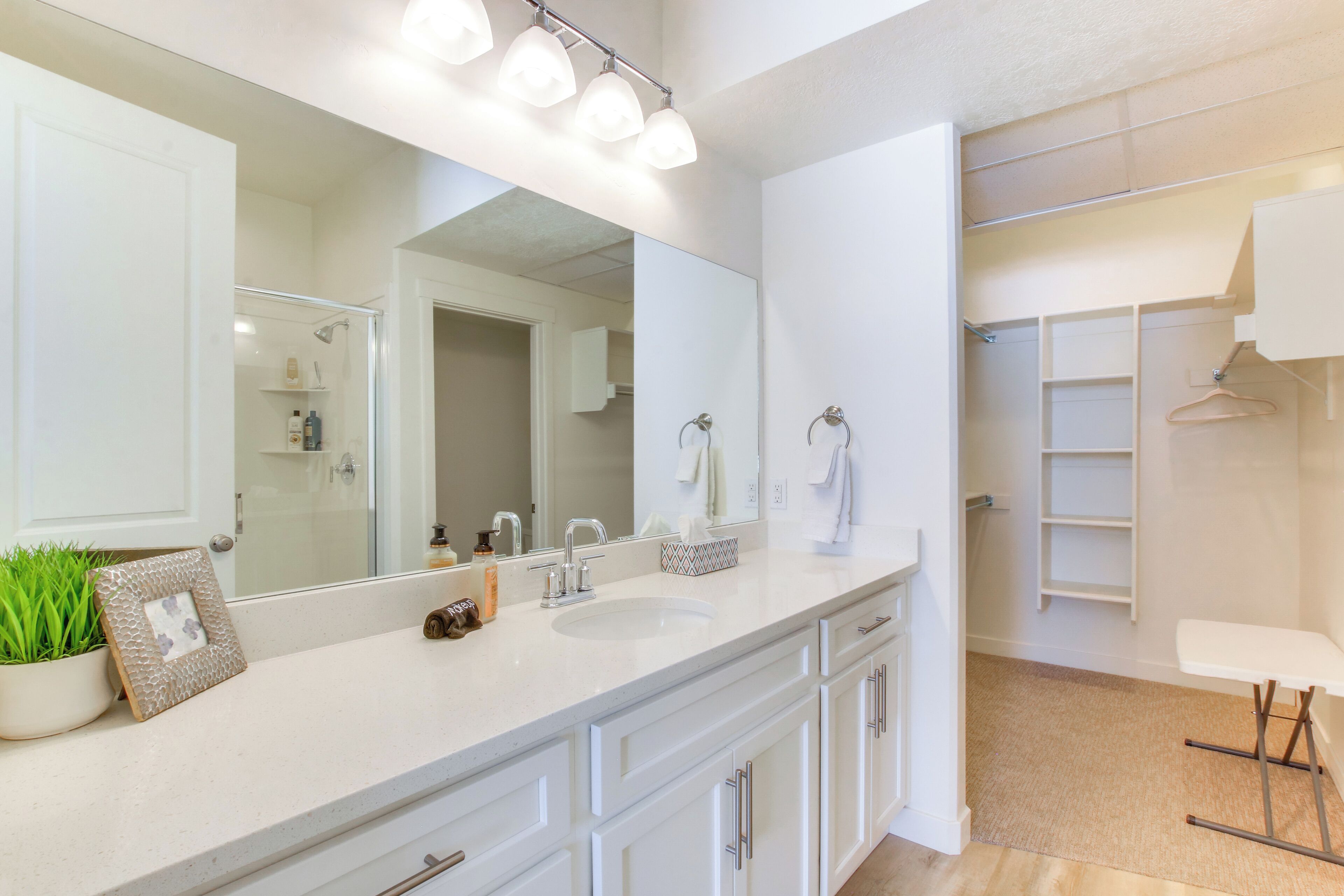 A modern bathroom with a large mirror, white cabinetry, a sink, and a shower area.