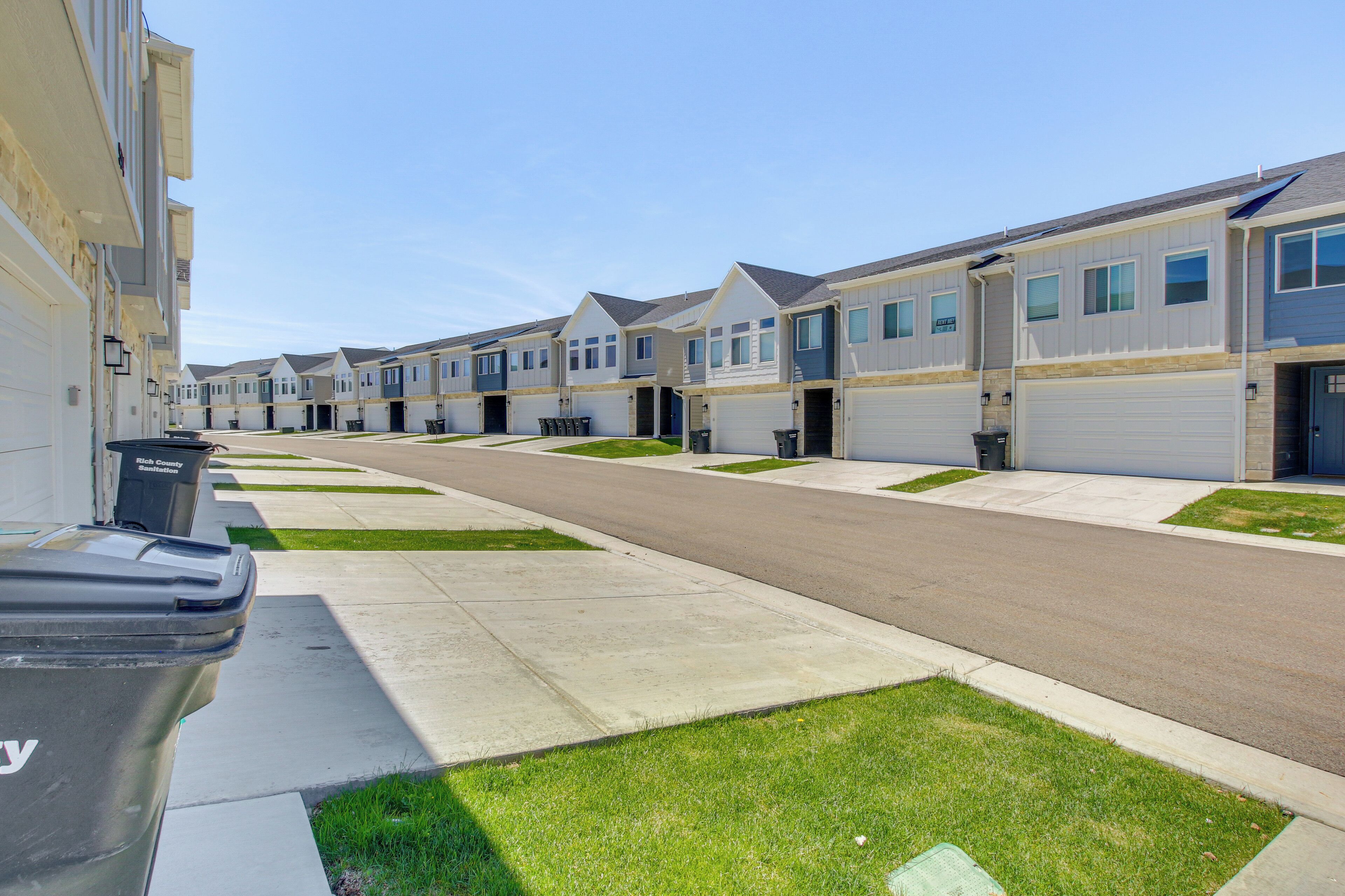 A row of townhouses with attached garages, a clear sidewalk, and a trash bin.