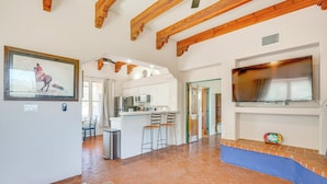 A spacious living area with exposed wooden beams, a kitchen with modern appliances, and a large flat-screen TV mounted on the wall.