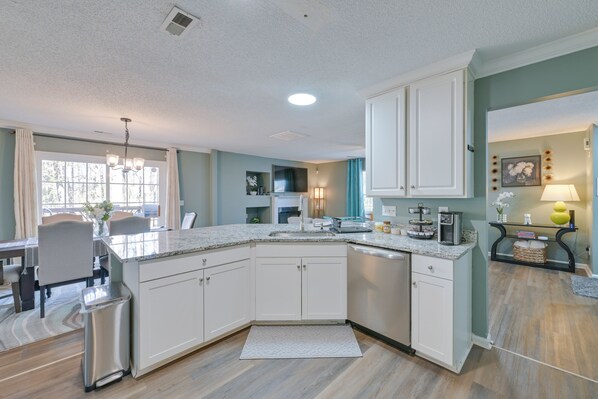 A modern kitchen with white cabinets, a granite countertop, and a dining area with a table and chairs.