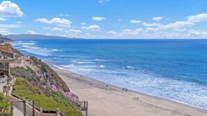 Un hôtel en bord de mer offrant une vue sur la plage, avec un escalier menant à la plage et un ciel dégagé.