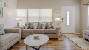 Un soggiorno con un divano beige, due tavolini con lampade, un tavolino rotondo e una porta con una vetrata decorata.