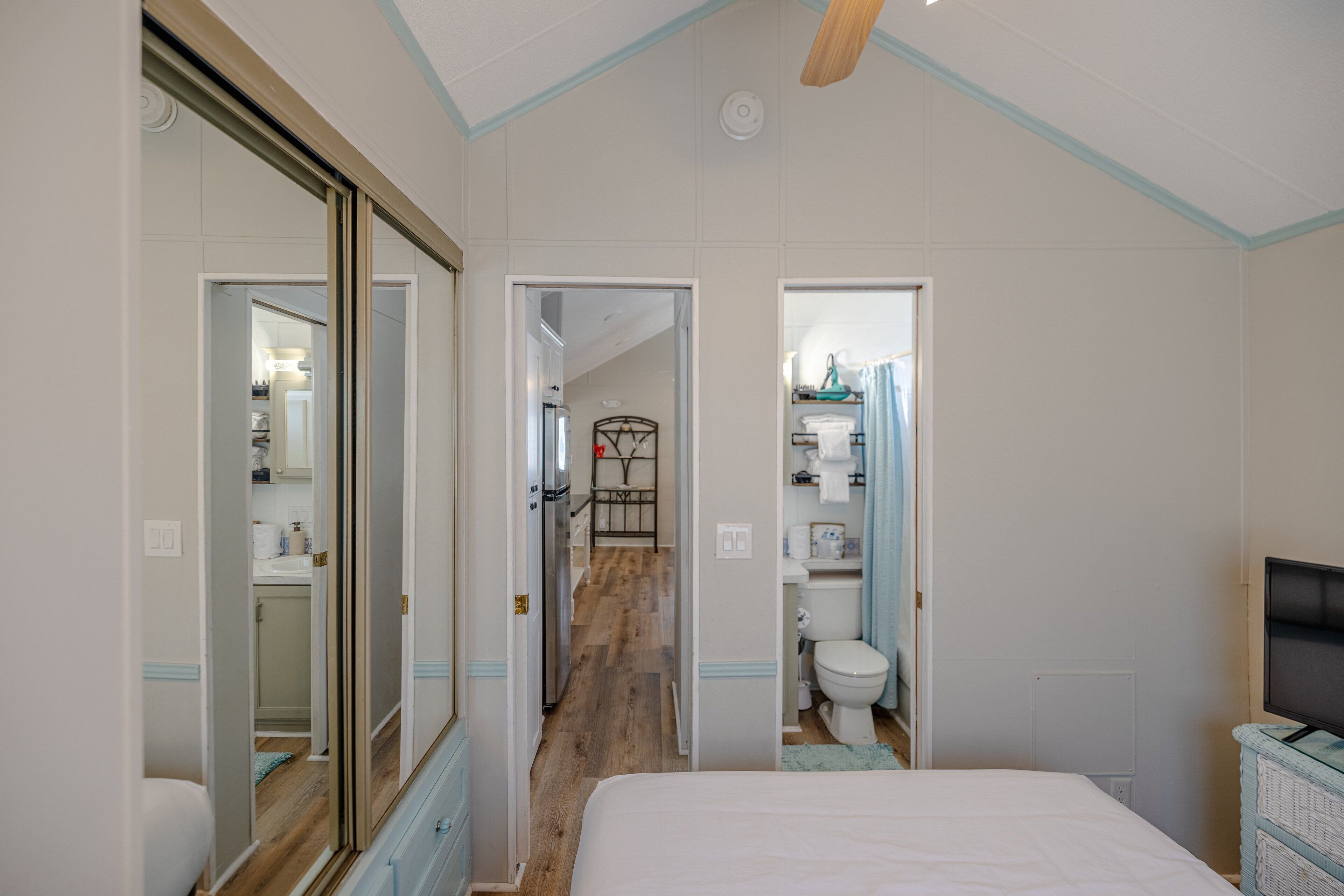 A bedroom with a large bed, a television, and a wardrobe. There is a bathroom with a toilet and a sink visible through an open door.