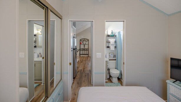 Un dormitorio con una cama grande, un televisor y un armario. Se ve un baño con un inodoro y un lavamanos a través de una puerta abierta.