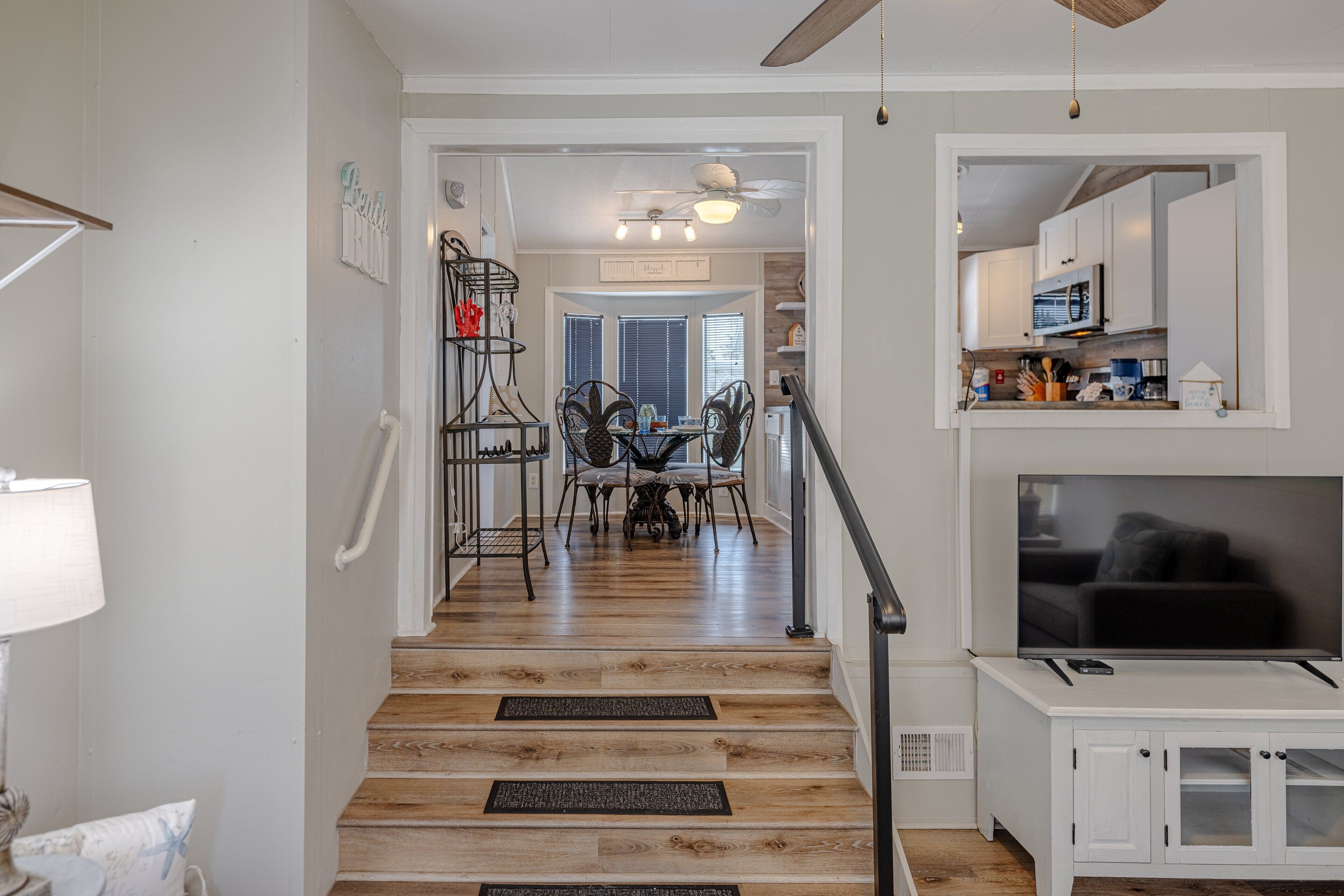 A staircase leading to a dining area with a ceiling fan, a television, and a kitchen area with cabinets and appliances.