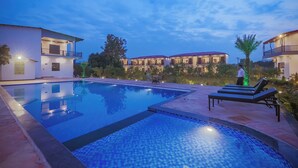 Une piscine entourée de bâtiments dotés de balcons et d’un éclairage extérieur, avec des chaises longues et une petite table à proximité.