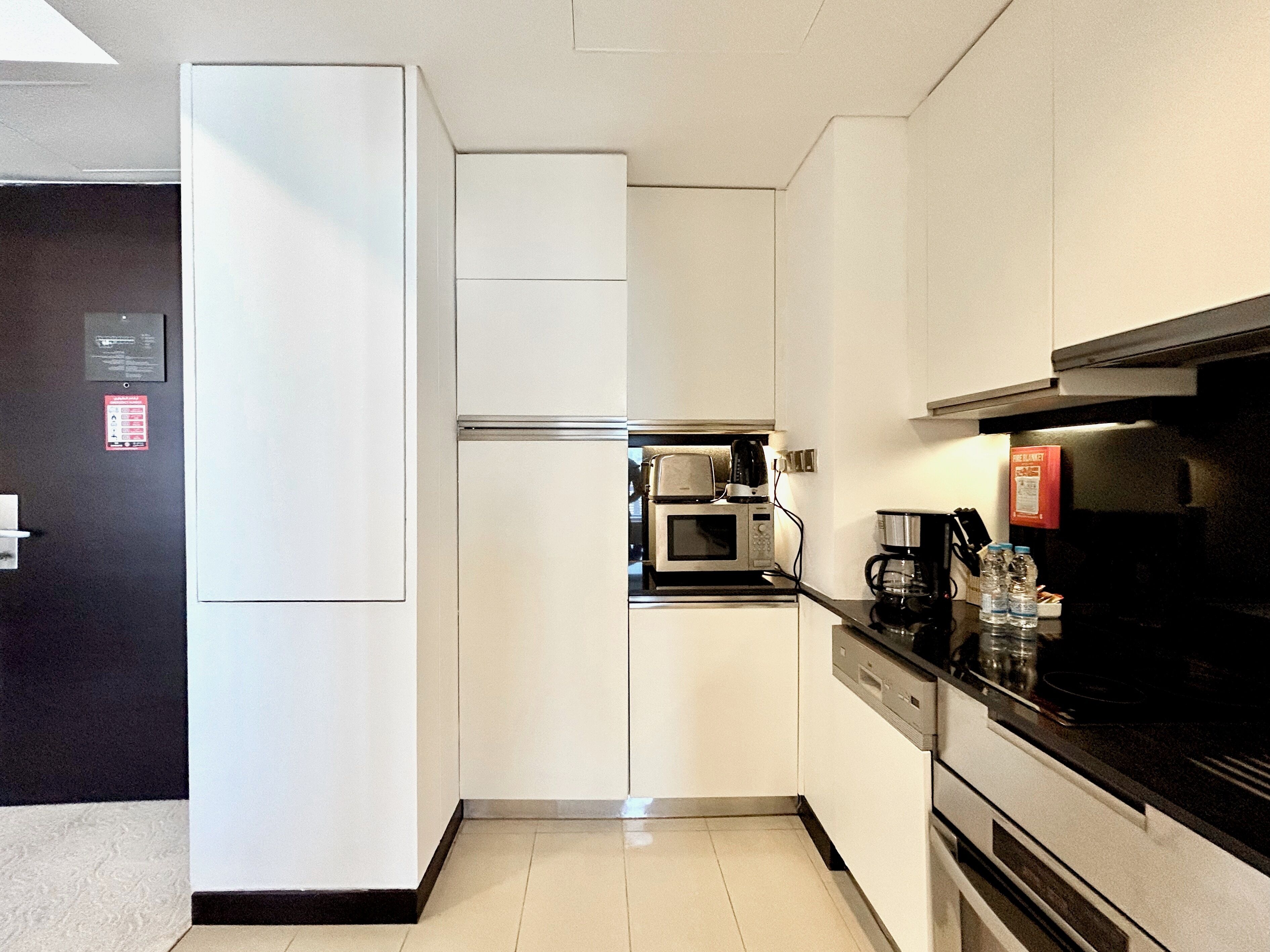 A compact kitchen with white cabinets, a microwave, a coffee maker, and a refrigerator.
