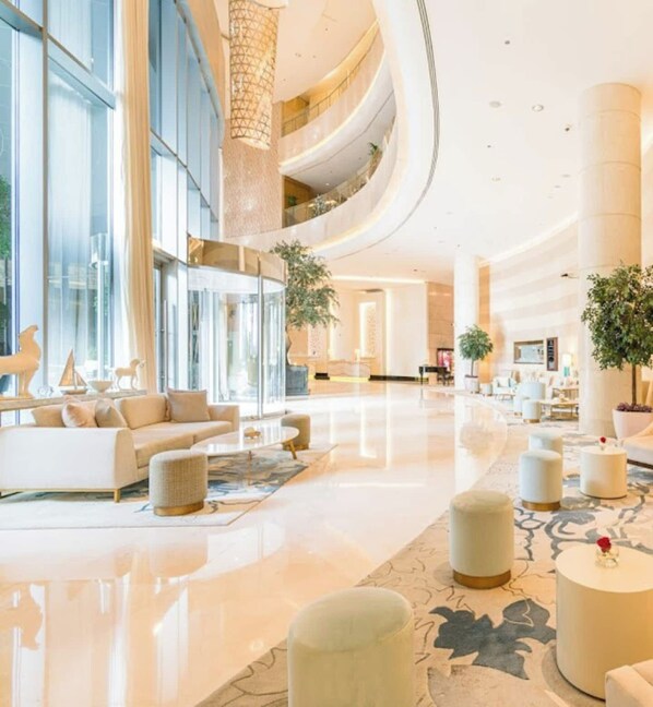 A spacious lobby with a high ceiling, large windows, and a central seating area with a sofa and ottomans.