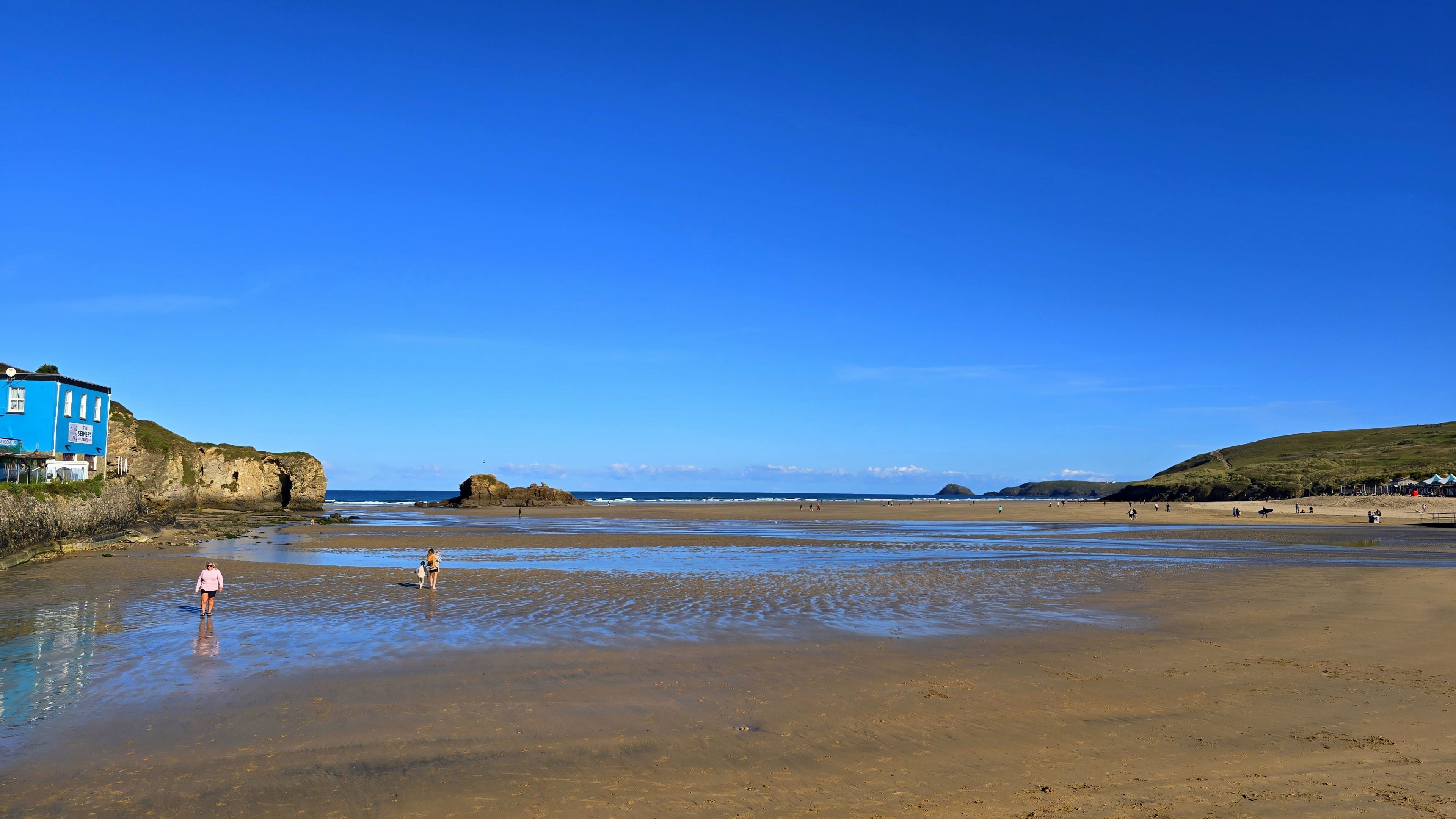 A beach with a blue building on the left, clear skies, and calm waters.