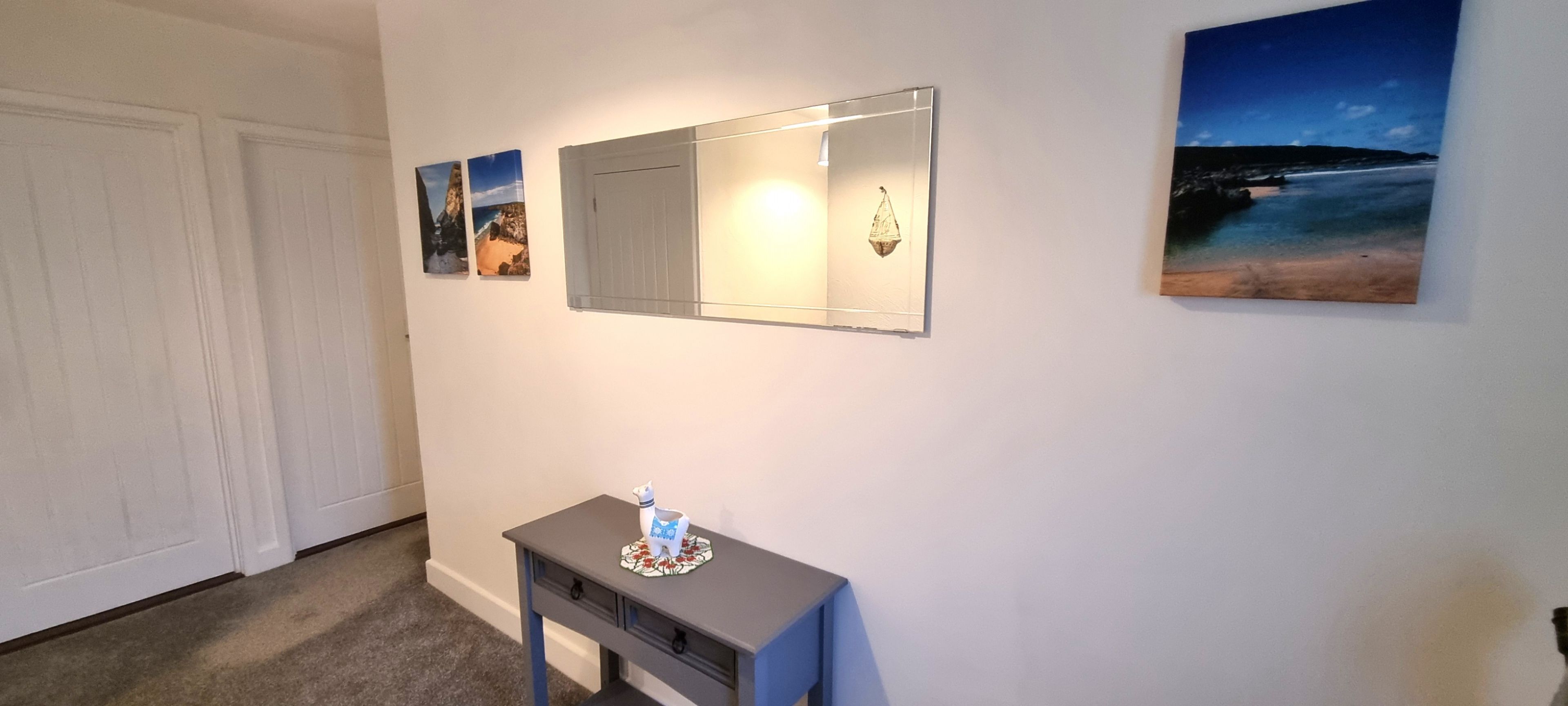 A hallway with a gray console table, a mirror, and two framed pictures on the wall.