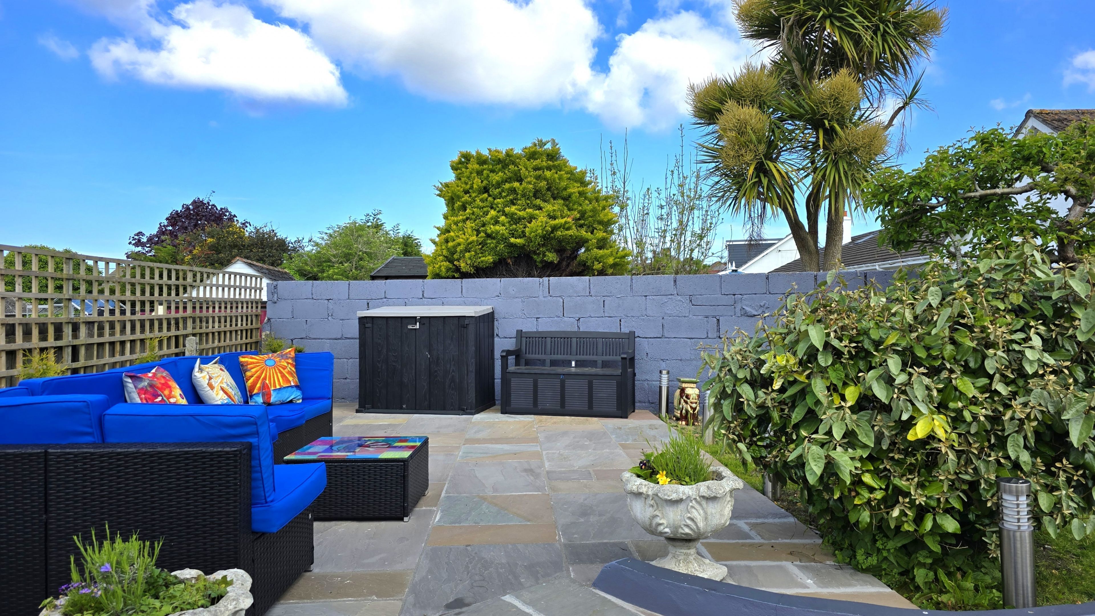 Eine Terrasse mit einer blauen Couch, einer schwarzen Bank und einer Steinmauer.
