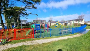 Ein Spielplatz mit verschiedenen Spielgeräten, einem roten Zaun und einer Rasenfläche.