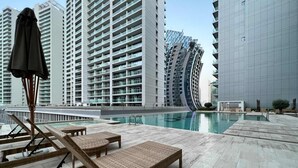Un espace piscine aménagé sur le toit, avec des chaises longues et une piscine, le tout entouré de grands immeubles.