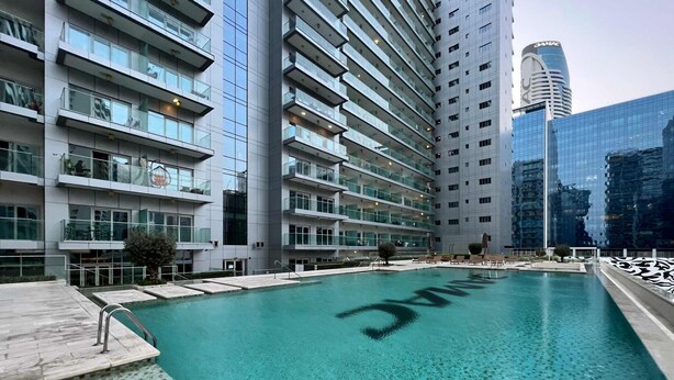 Un bâtiment moderne doté d’une piscine, de balcons en verre et offrant une vue sur d’autres immeubles de grande hauteur.