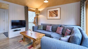 A cozy living room with a wooden ceiling, a grey sofa with patterned cushions, a wooden coffee table, and a flat-screen TV mounted on the wall. - Host Stay Strength (Wareham)