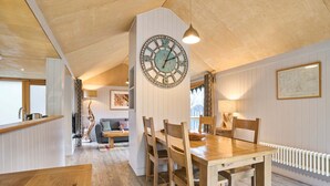 A dining area with a wooden table and chairs, a large wall clock, and a cozy seating area with a sofa and cushions. - Host Stay Strength (Wareham)