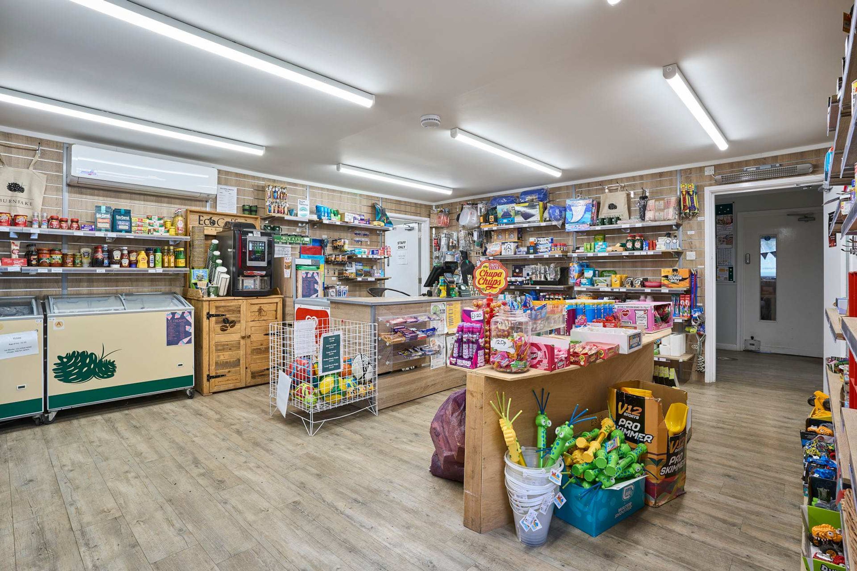 A well-lit store with various shelves stocked with products, a refrigerated display, and a checkout counter.