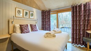 Un dormitorio con una cama grande, cabecera de madera, obra de arte con hojas enmarcadas y una ventana con cortinas.